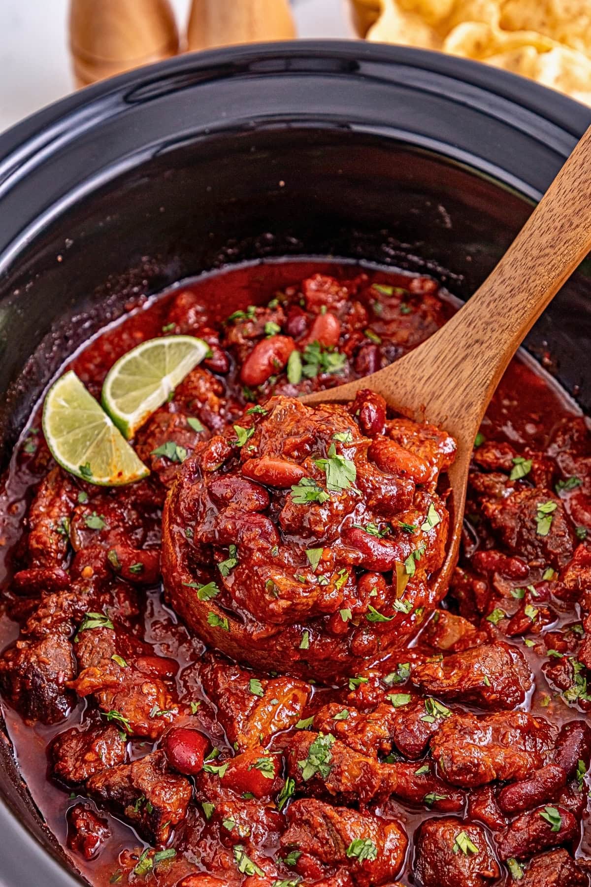 Hearty chili with beans in a slow cooker, garnished with lime and herbs.