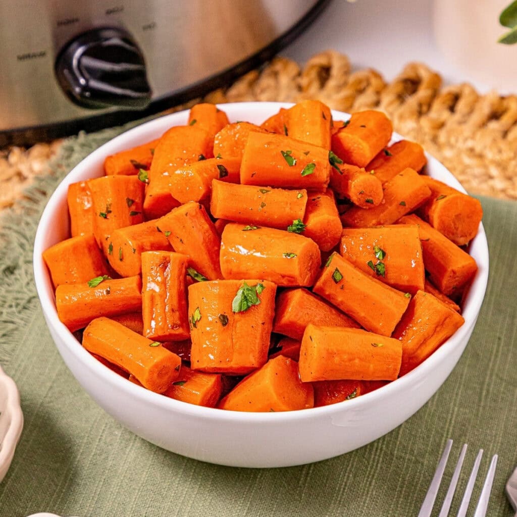 White bowl filled with glazed carrot pieces, garnished with chopped herbs.
