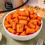 White bowl filled with glazed carrot pieces, garnished with chopped herbs.