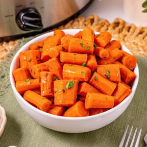White bowl filled with glazed carrot pieces, garnished with chopped herbs.