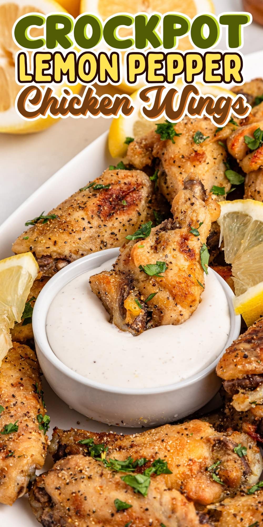 Chicken wings with lemon wedges and dip on a white plate.