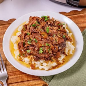Shredded beef with gravy on mashed potatoes, garnished with chopped parsley.