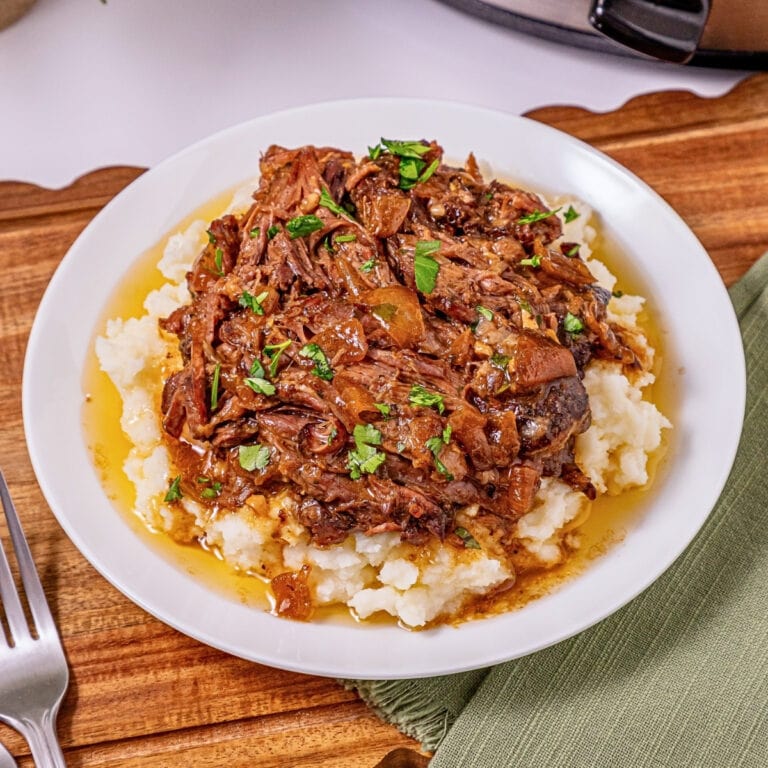 Shredded beef with gravy on mashed potatoes, garnished with chopped parsley.