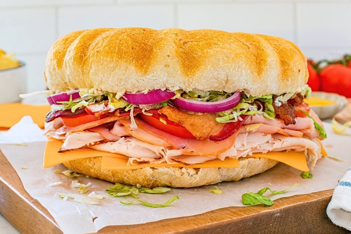 Large sandwich with turkey, cheese, bacon, lettuce, tomato, and red onion.