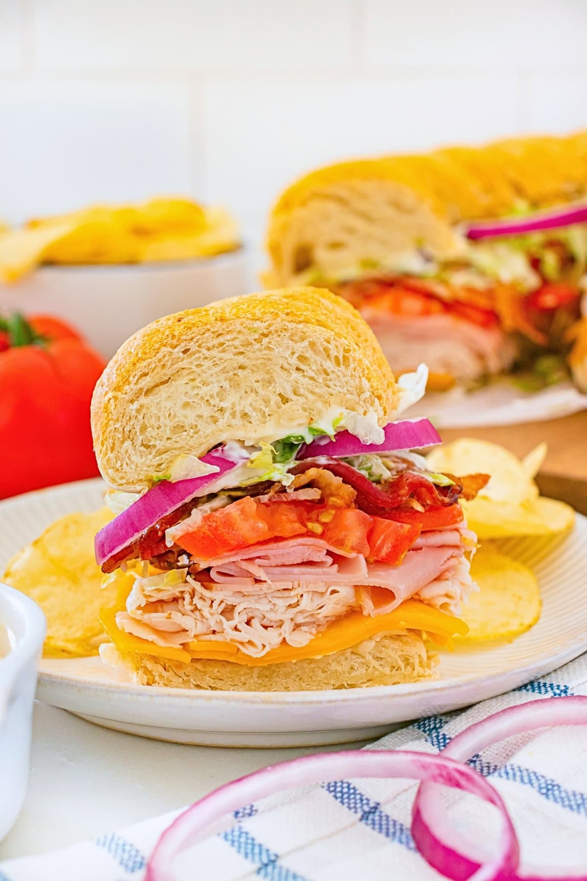 Turkey sandwich with lettuce, tomato, onion, and chips on a white plate.
