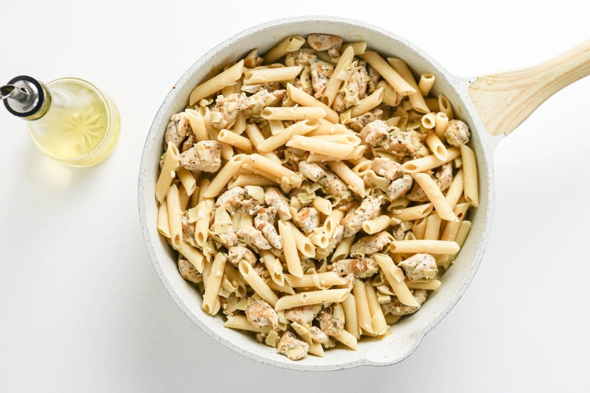 Penne pasta and chicken in a white skillet, with a bottle of olive oil nearby.