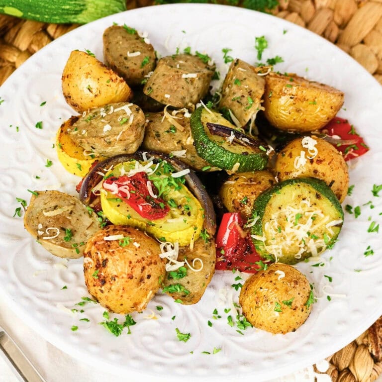 Roasted potatoes, sausage, zucchini, and peppers on a white plate with herbs.