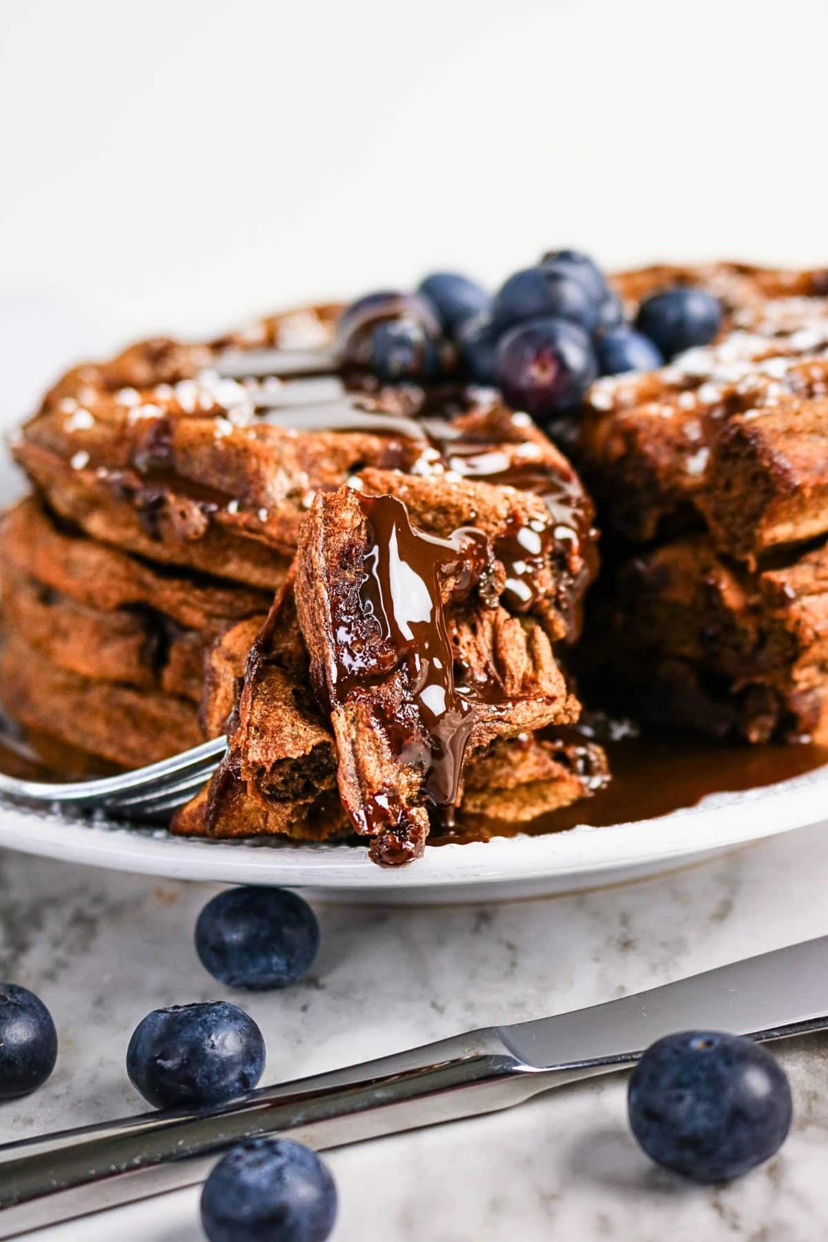 Stack of chocolate waffles with blueberries and syrup, with one bite on a fork.