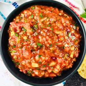 A bowl of chunky tomato salsa with herbs and vegetables.