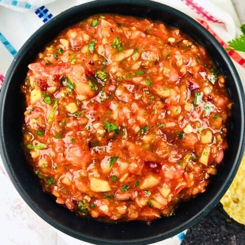 A bowl of chunky tomato salsa with herbs and vegetables.