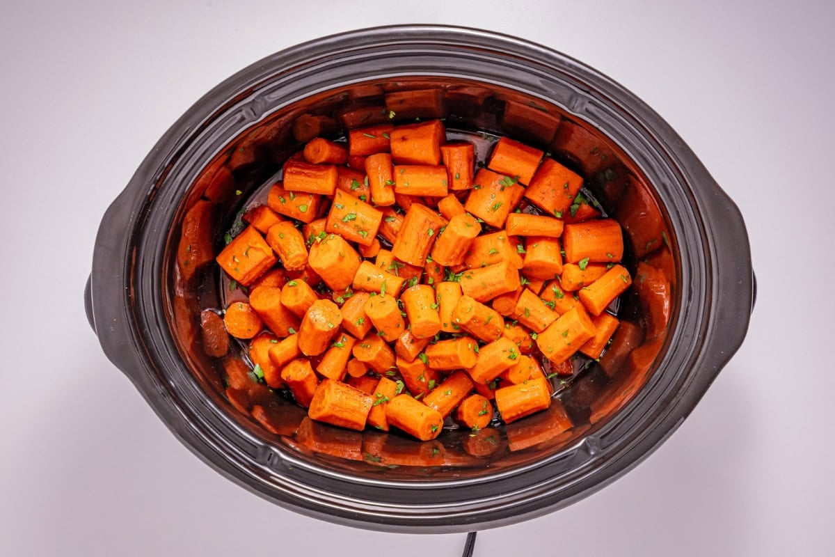 Chopped carrots in a slow cooker, seasoned with herbs.