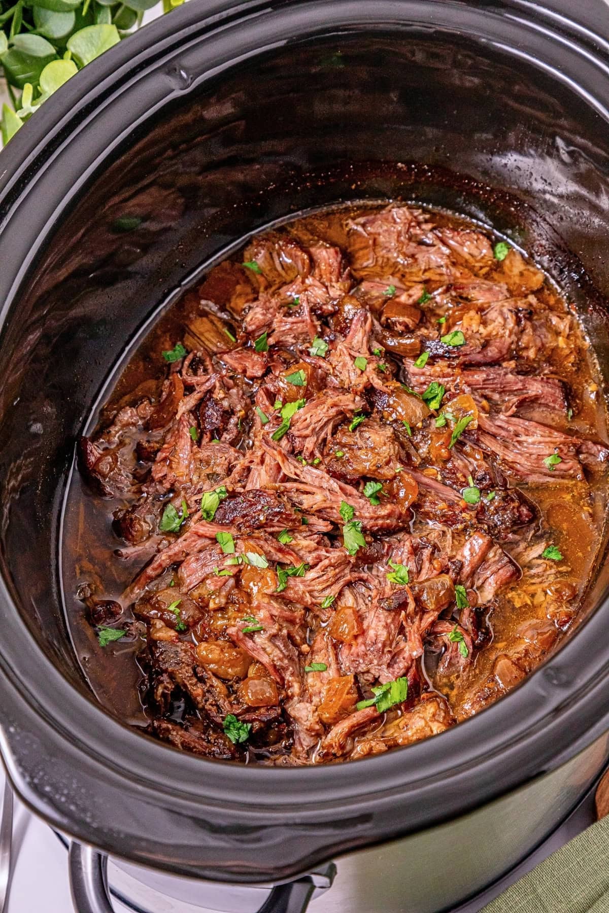 Shredded beef with sauce and herbs in a black slow cooker.