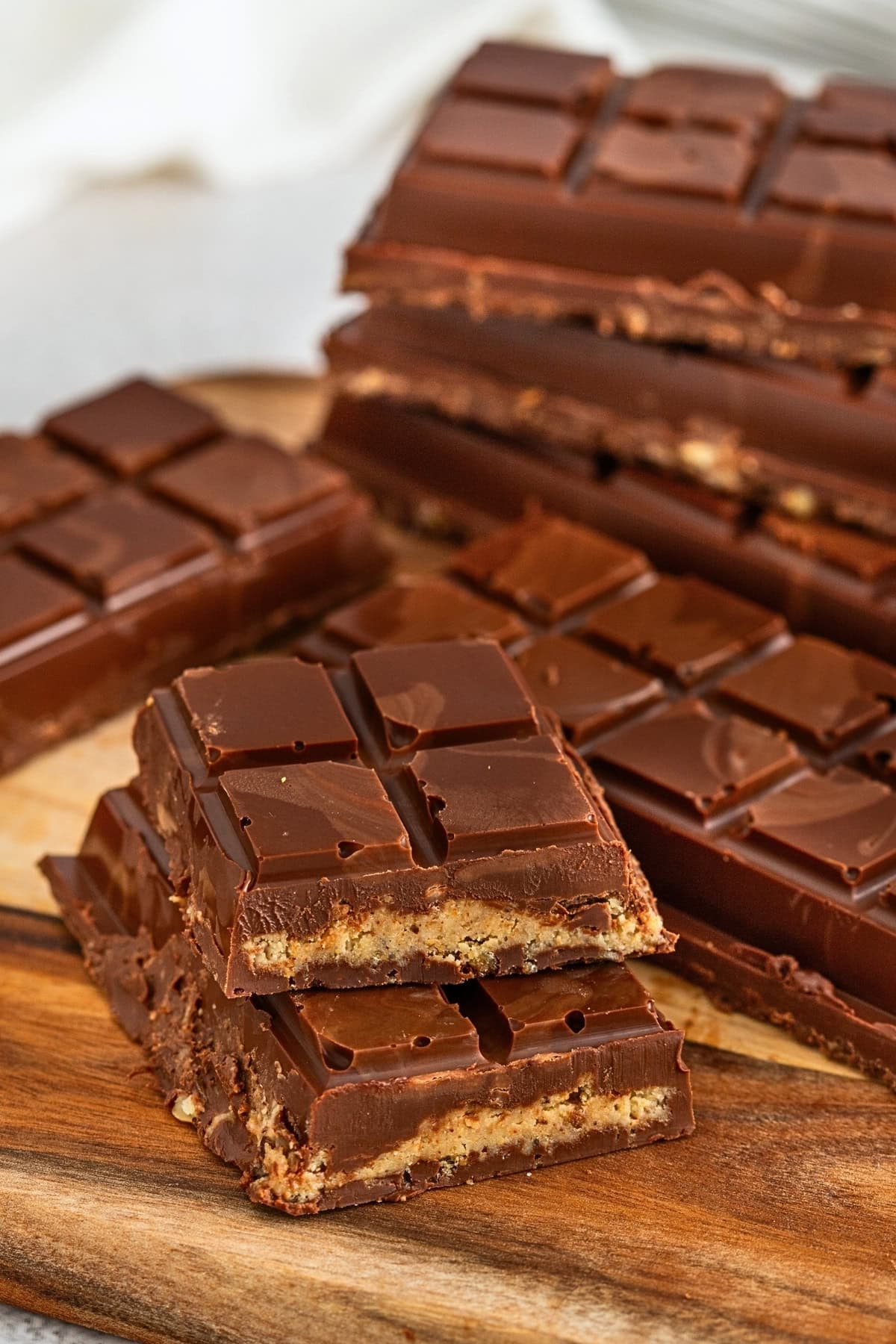 Chocolate bars with a cookie layer stacked on a wooden cutting board.