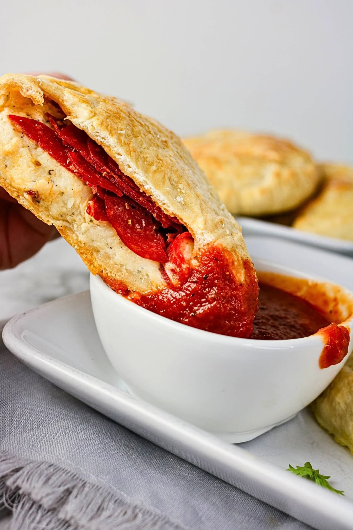 A calzone being dipped into marinara sauce on a white plate.