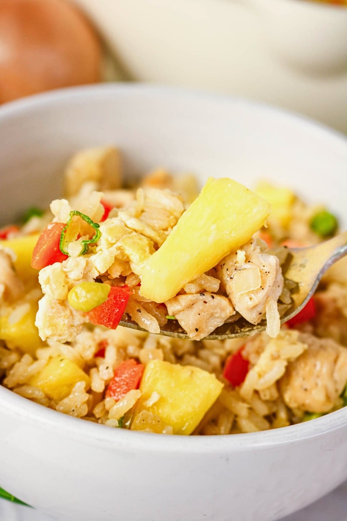 A fork holds pineapple fried rice with chicken, red pepper, and green onions.