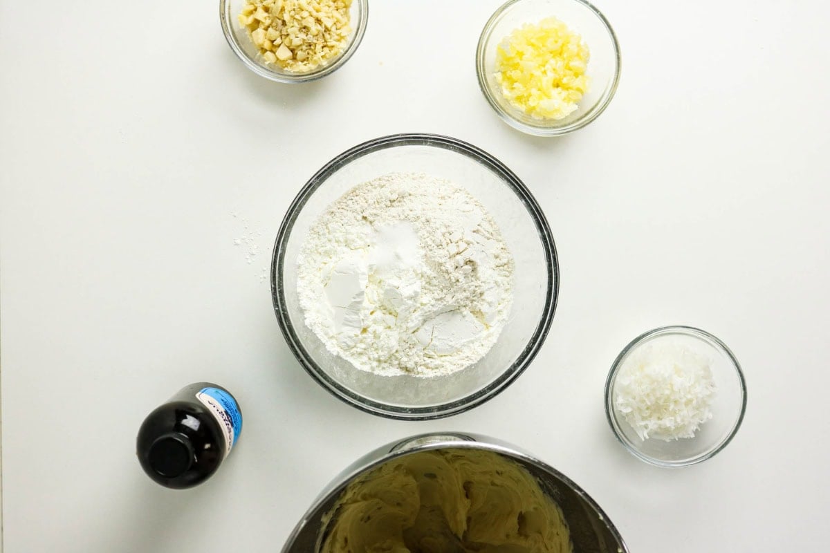 Flour, sugar, baking powder in bowl; nuts, pineapple, coconut, vanilla nearby.