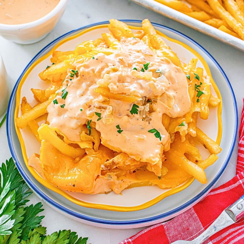 French fries topped with melted cheese and creamy sauce, garnished with parsley.