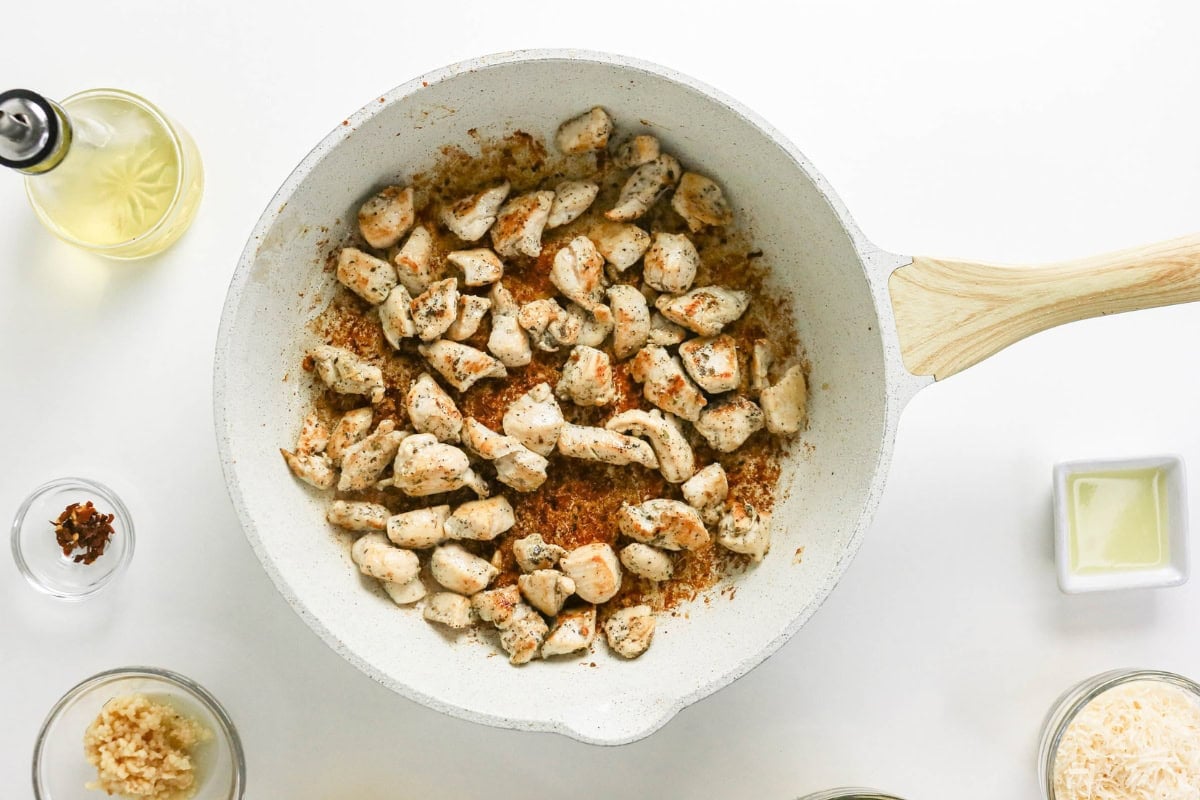 Cooked, seasoned chicken pieces in a white pan surrounded by small bowls of ingredients.