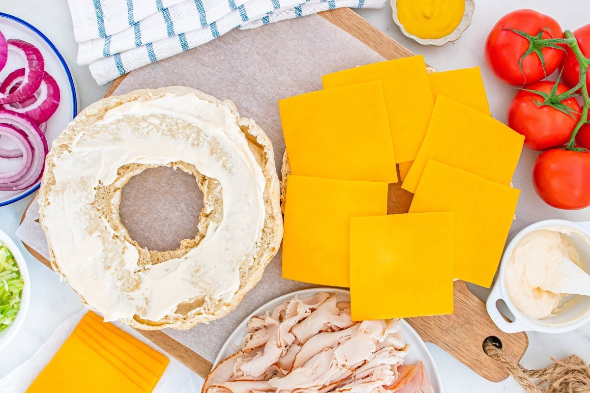 Sliced cheese, bagel, turkey, tomato, and sandwich fixings on a table.