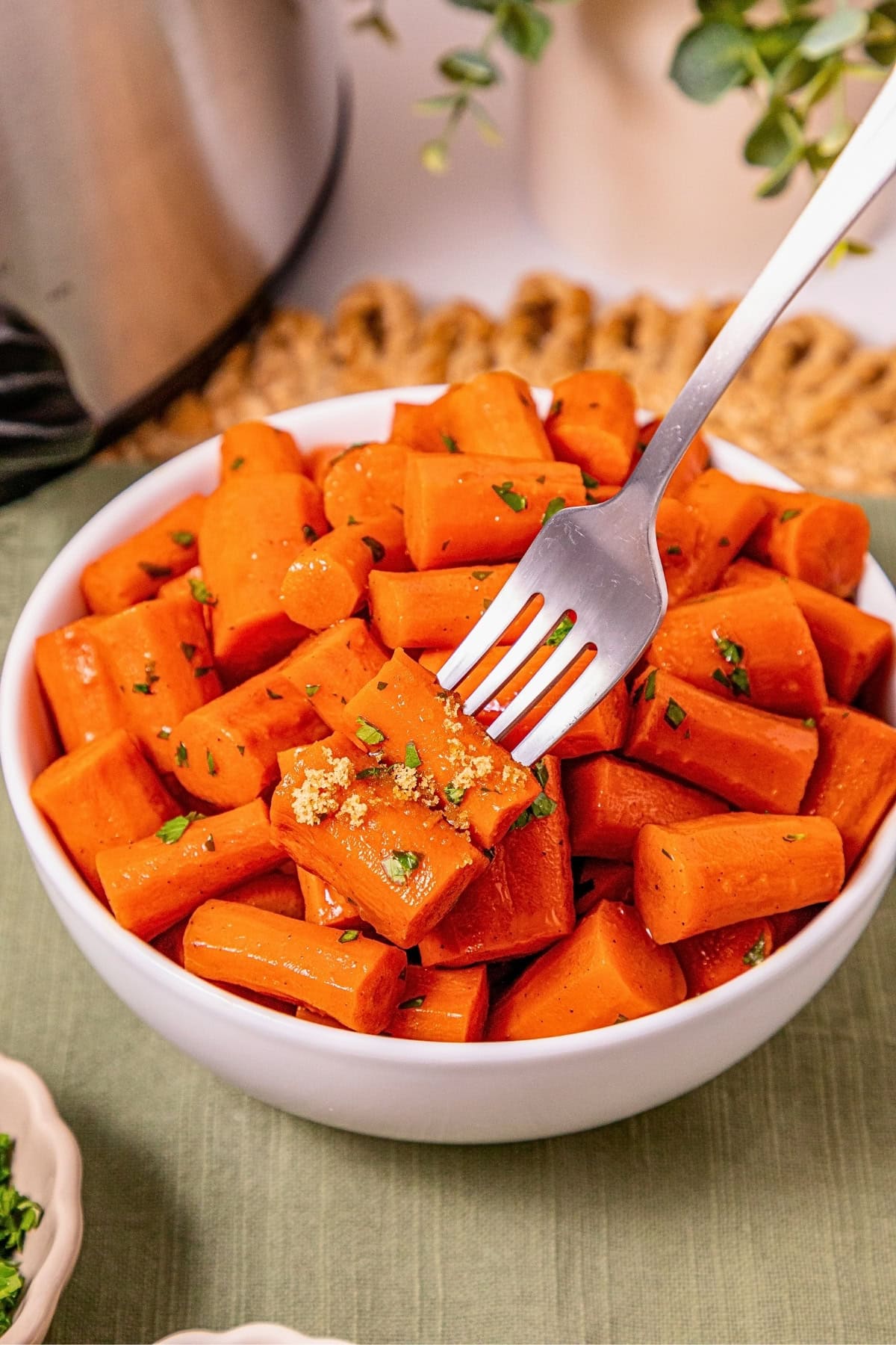 A fork holds glazed carrots over a bowl filled with cooked carrot pieces.
