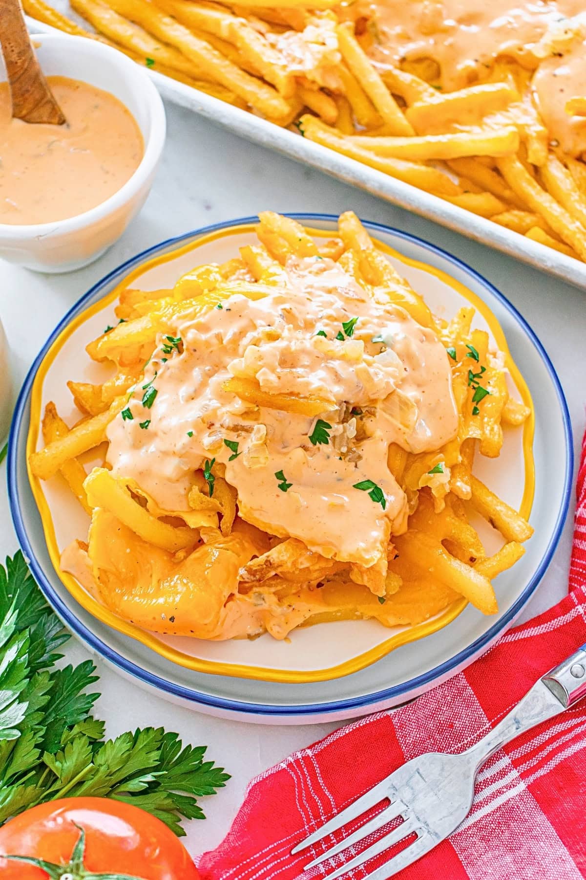 Cheesy fries topped with creamy sauce and herbs on a plate with a fork nearby.