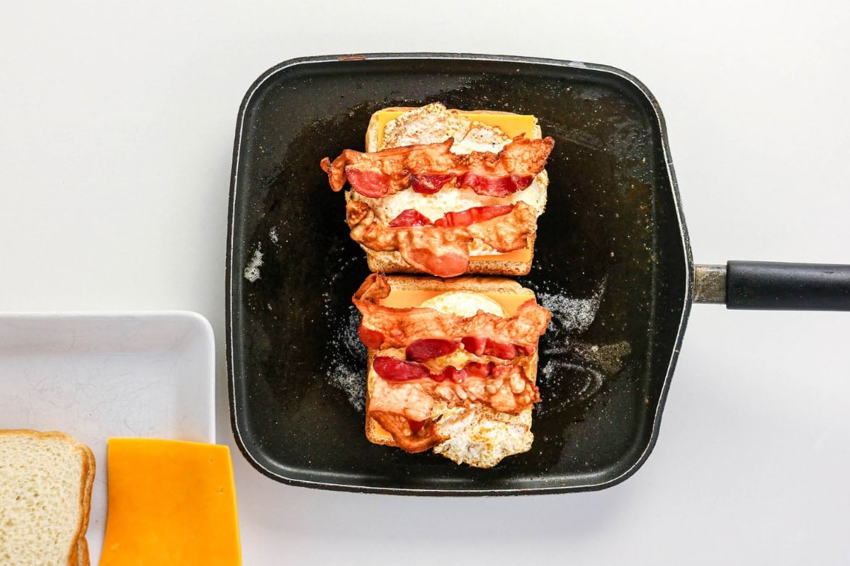 Two sandwiches with bacon, egg, and cheese in a frying pan.