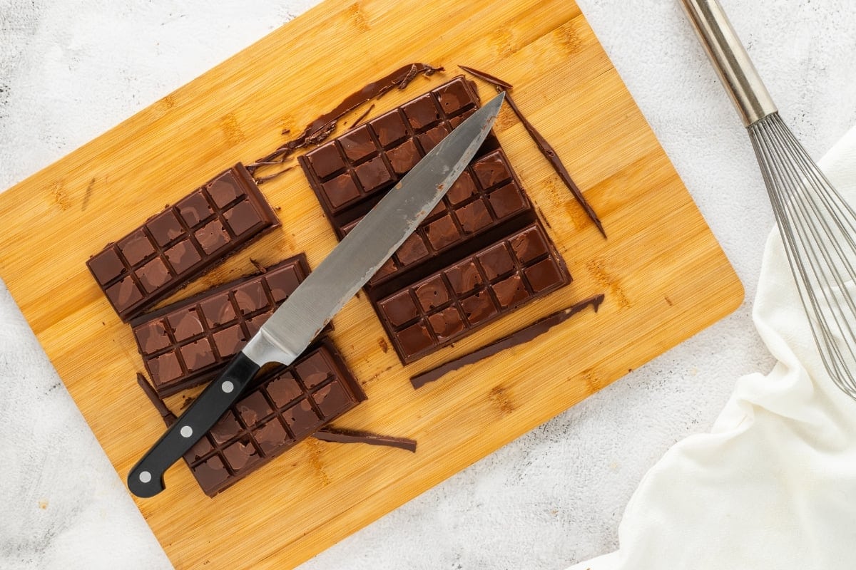 Chopped chocolate bars and a knife on a wooden cutting board.