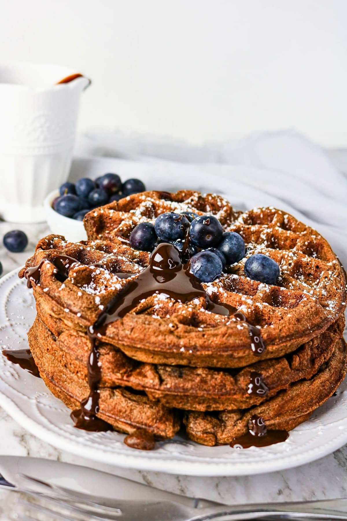 A stack of waffles topped with blueberries, chocolate sauce, and powdered sugar.