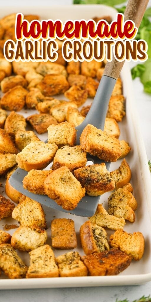 Spatula holding homemade garlic croutons above a baking tray.