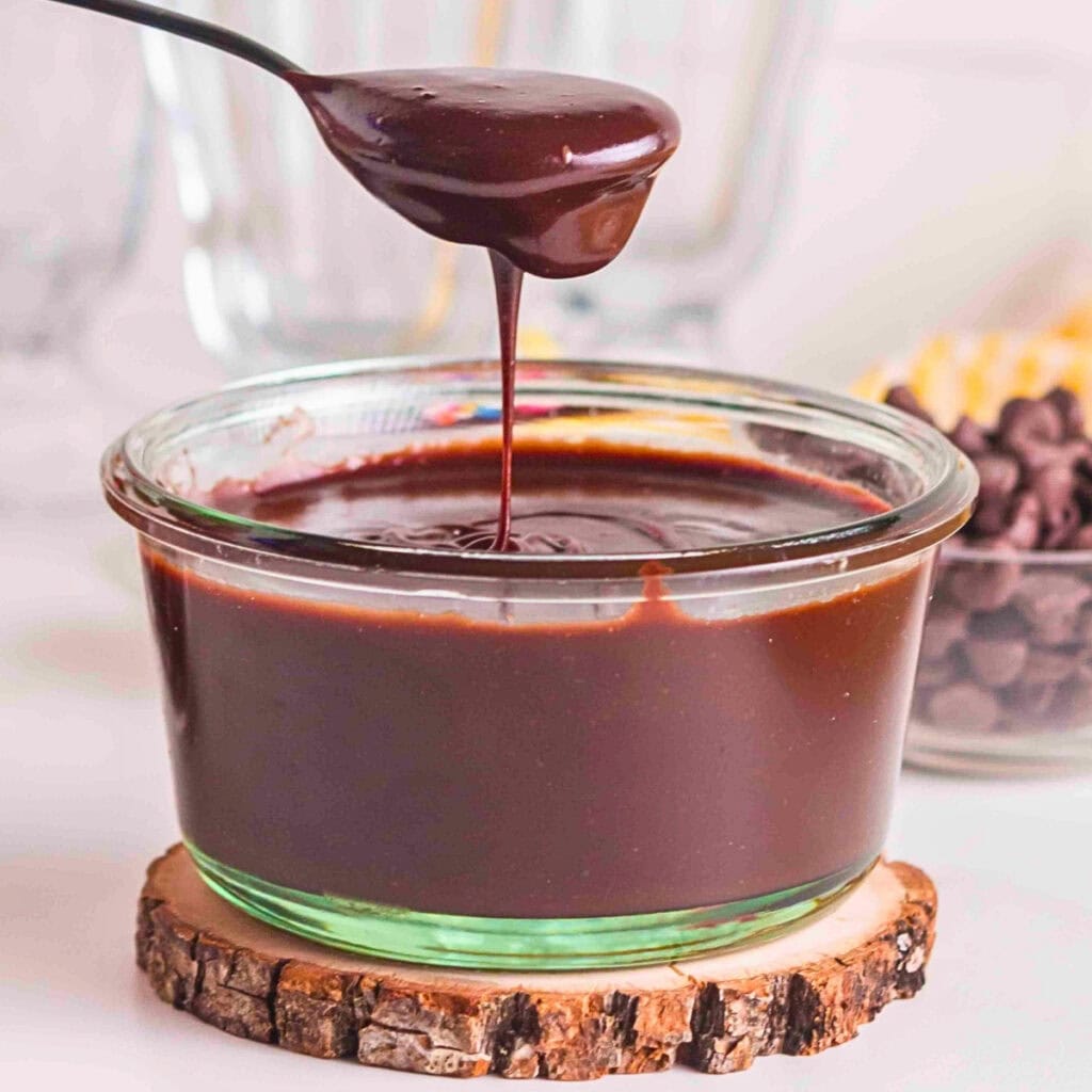 A spoon drizzles chocolate sauce into a glass bowl of chocolate sauce.