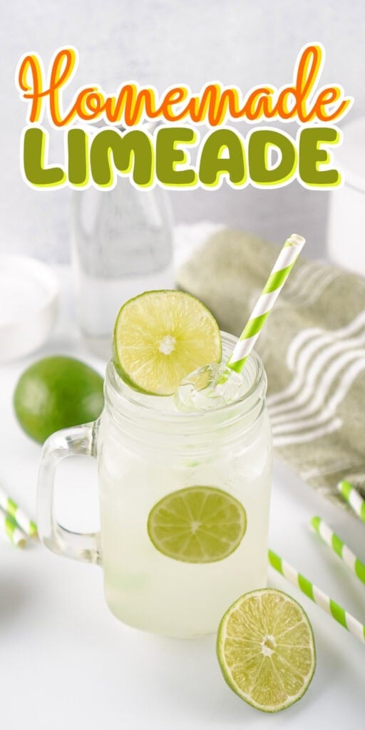 A mason jar of limeade with lime slices and a striped straw on a white table.