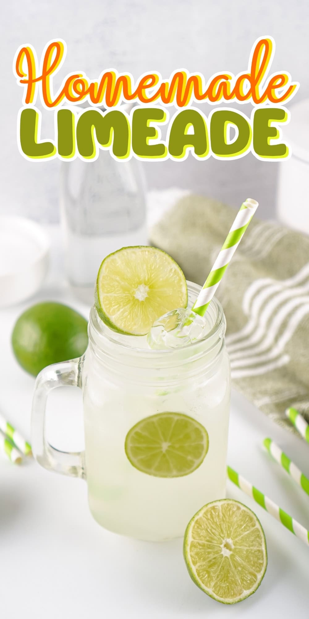A mason jar of limeade with lime slices and a striped straw on a white table.