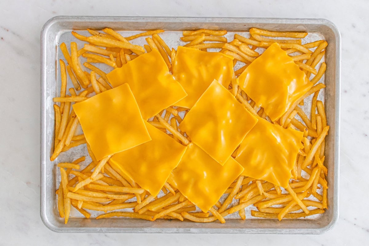 A tray of fries topped with slices of melted yellow cheese.