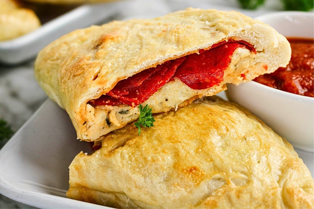 A calzone with pepperoni, cheese, and sauce on a white plate.