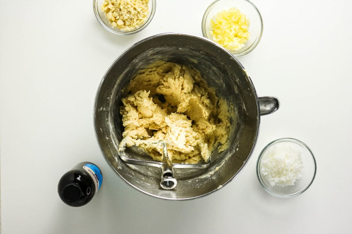 A mixing bowl with dough and three small bowls of baking ingredients nearby.