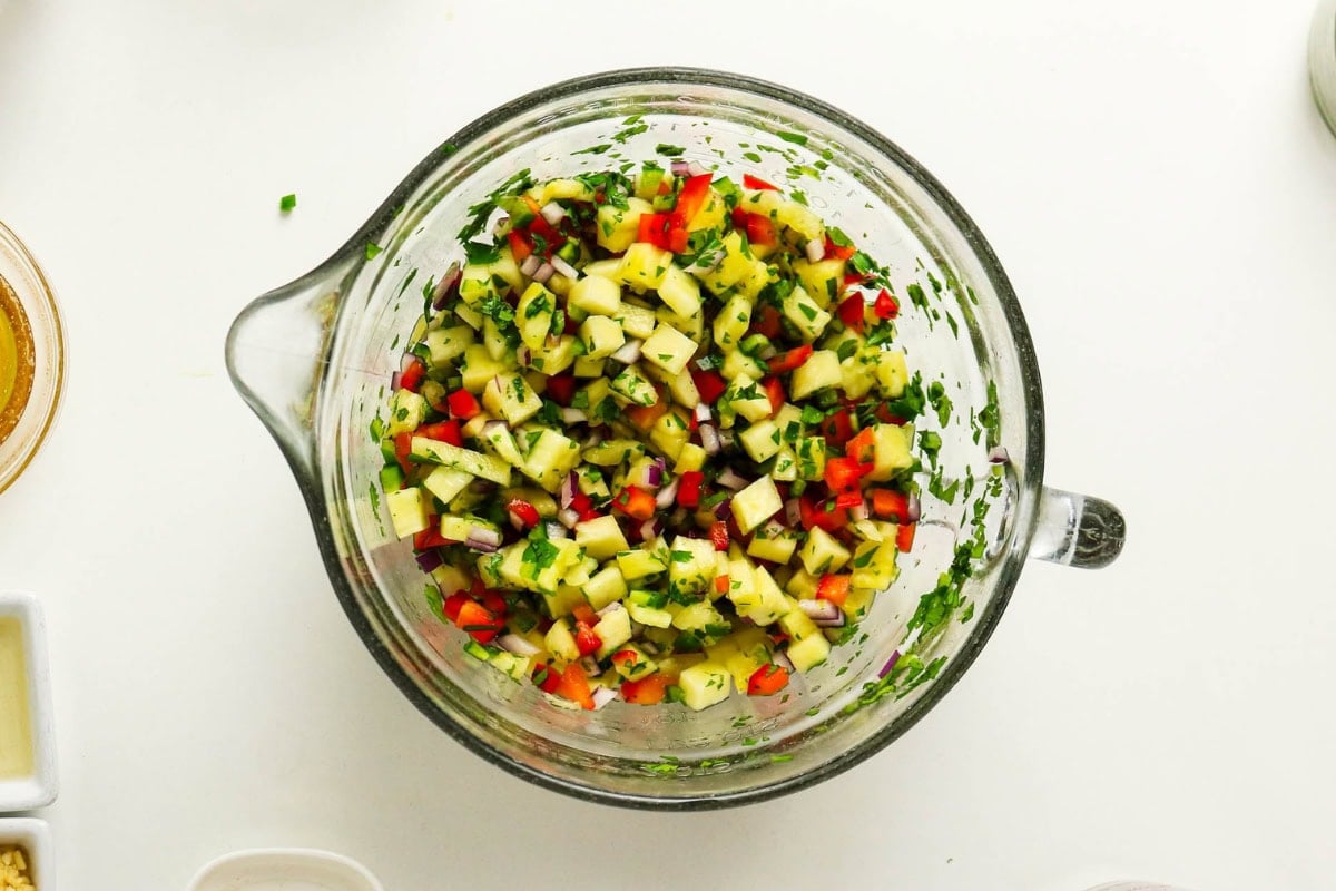 A glass bowl of colorful chopped vegetable salsa on a white surface.