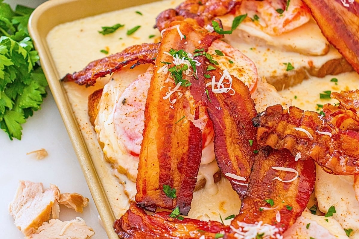 Crispy bacon on cheesy toast with herbs, served on a baking tray.