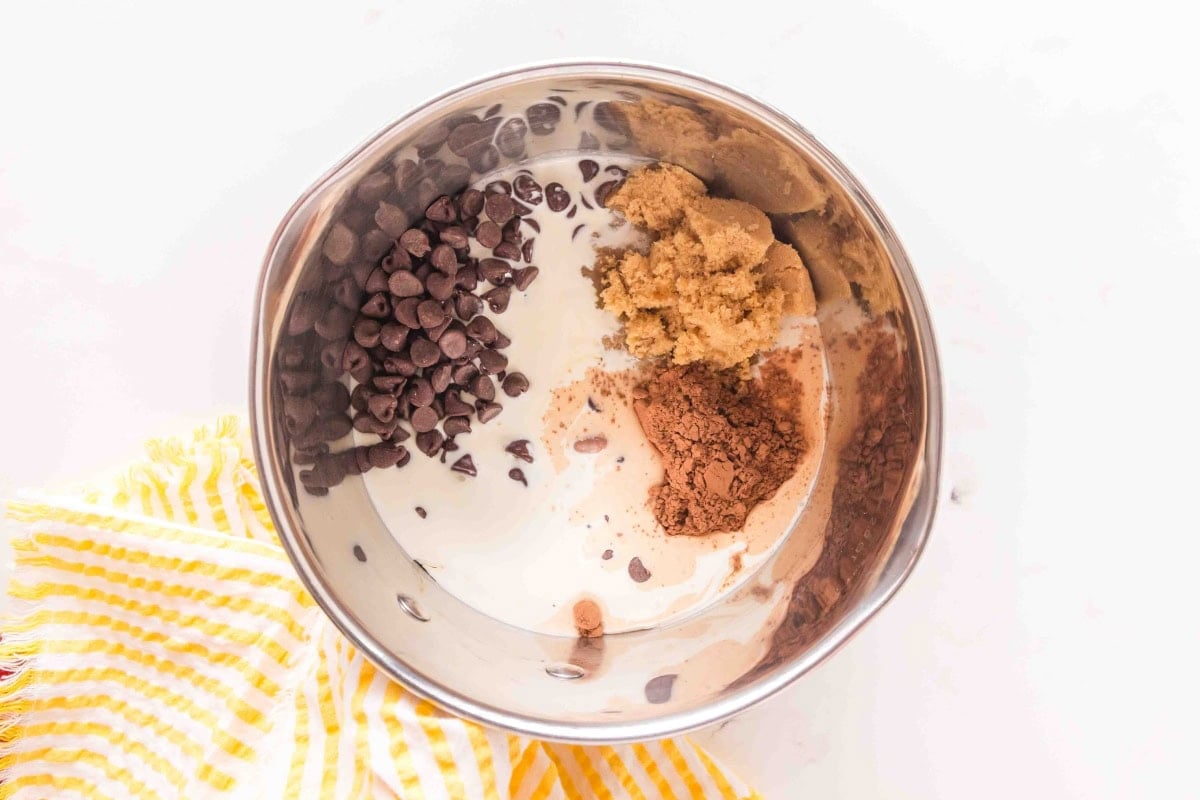 A mixing bowl with brown sugar, cocoa powder, chocolate chips, and milk.
