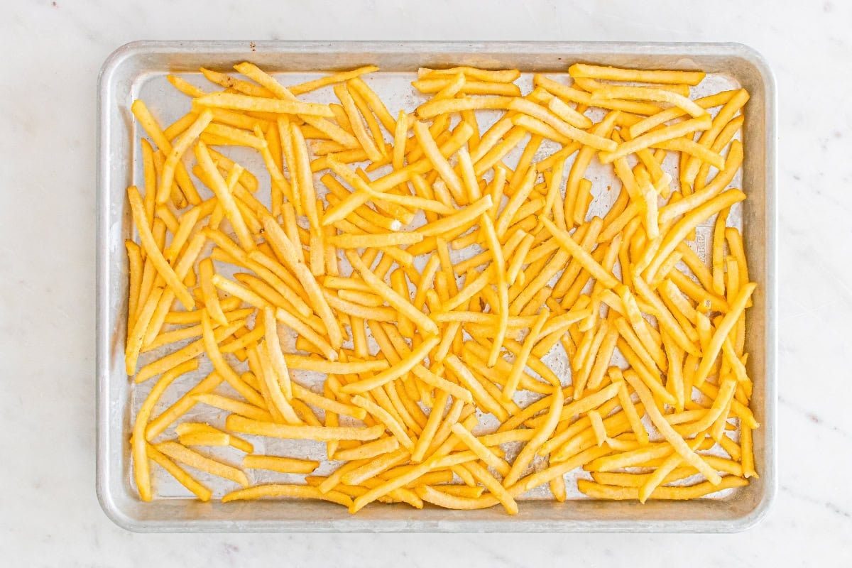 A baking tray scattered with uncooked French fries.