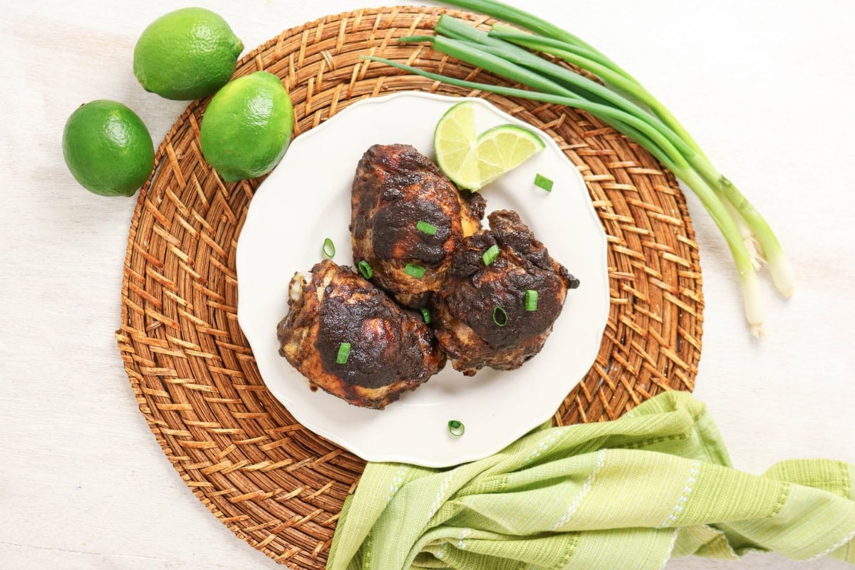 Three pieces of grilled chicken on a plate with limes and green onions.