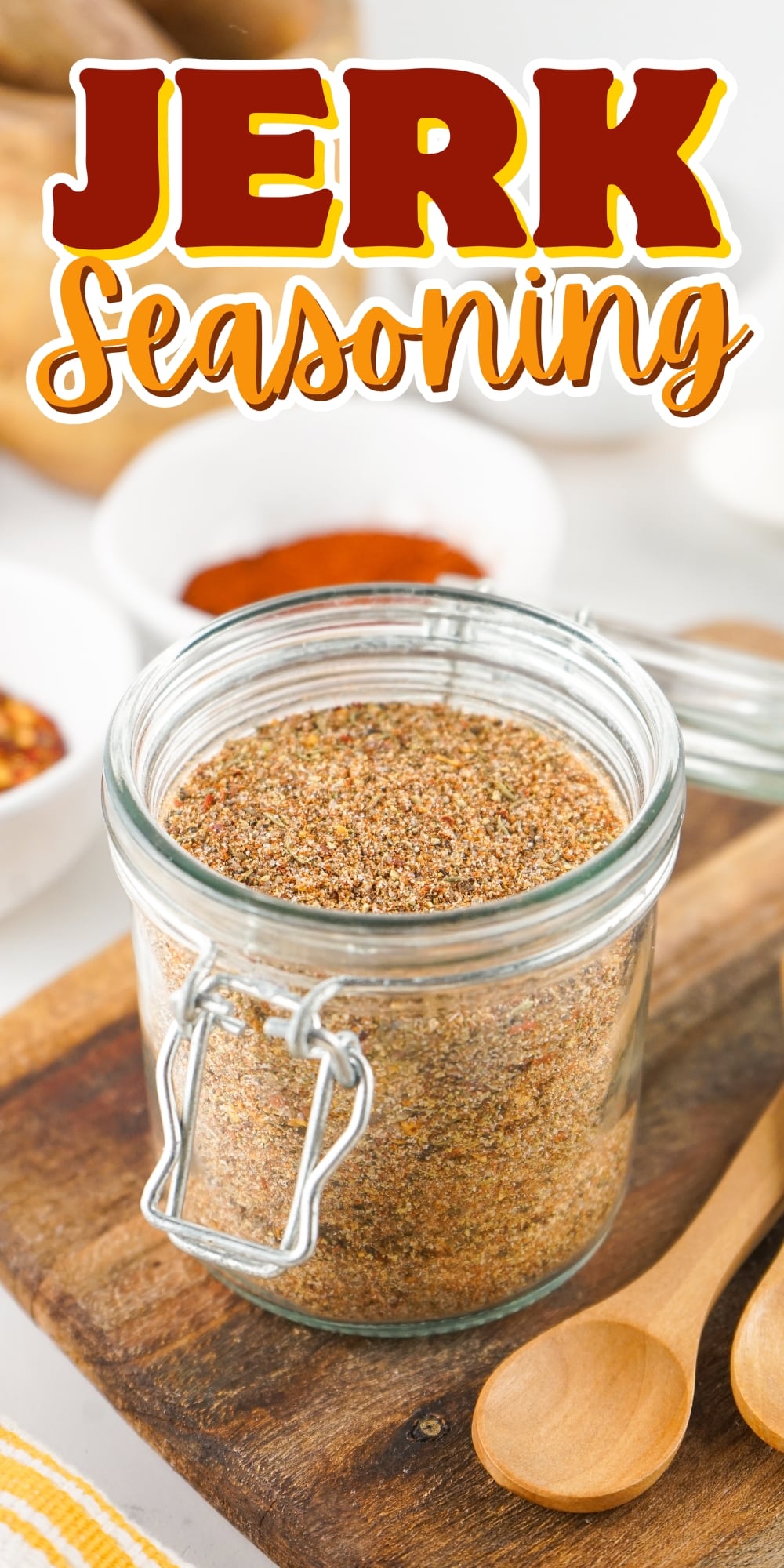 A jar of jerk seasoning on a wooden board with spoons and bowls nearby.