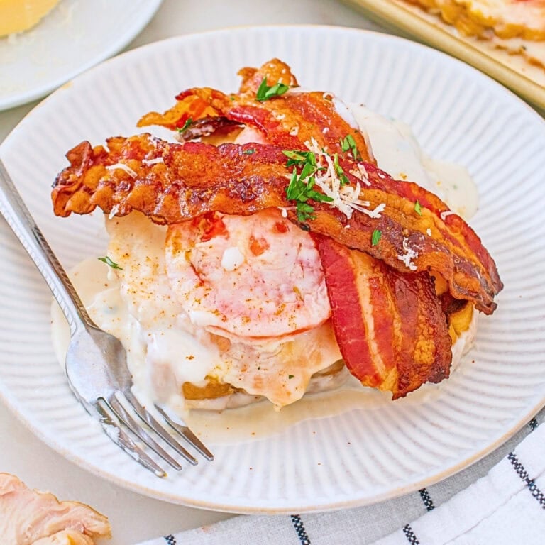 Open-faced sandwich with bacon, tomato, sauce, and herbs on a white plate.
