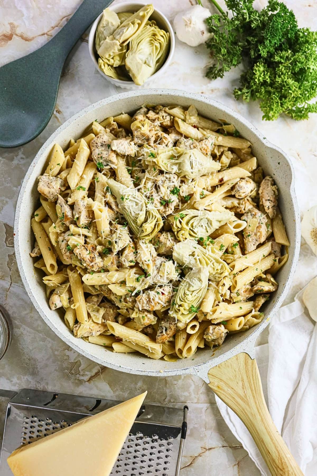 Penne pasta with chicken and artichokes garnished with herbs in a skillet.