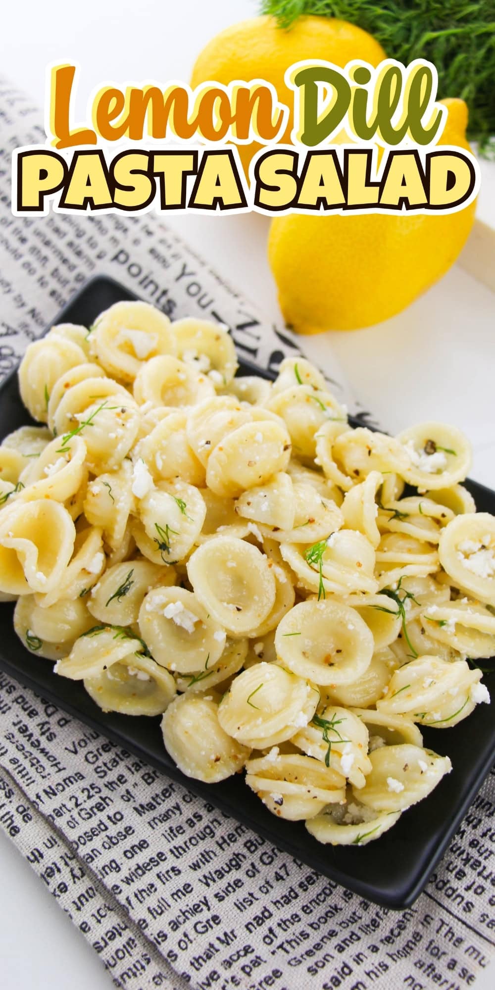 Orecchiette pasta salad with dill and feta on a black plate, lemons nearby.