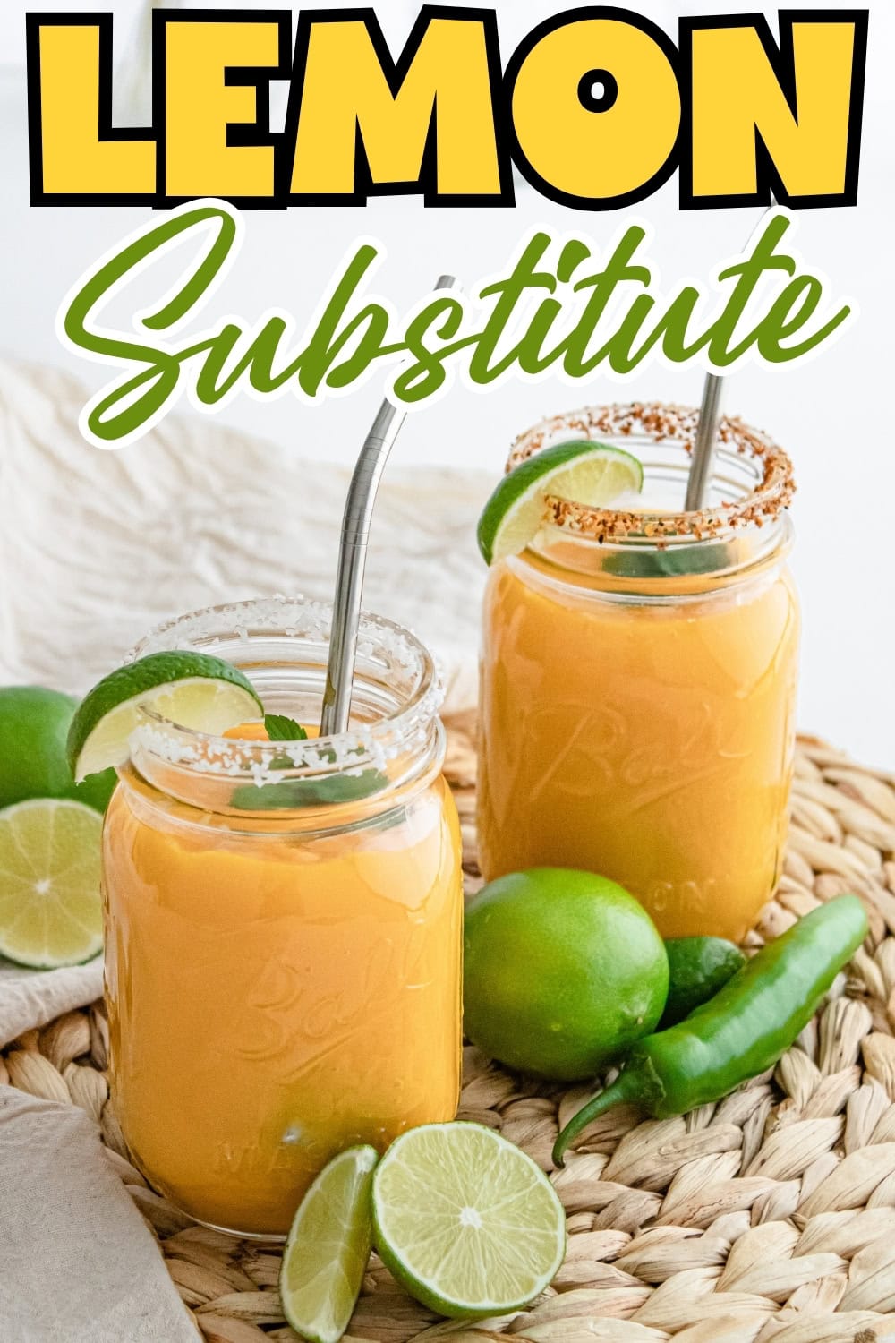 Two mason jars of orange drink with limes and metal straws on a woven mat.