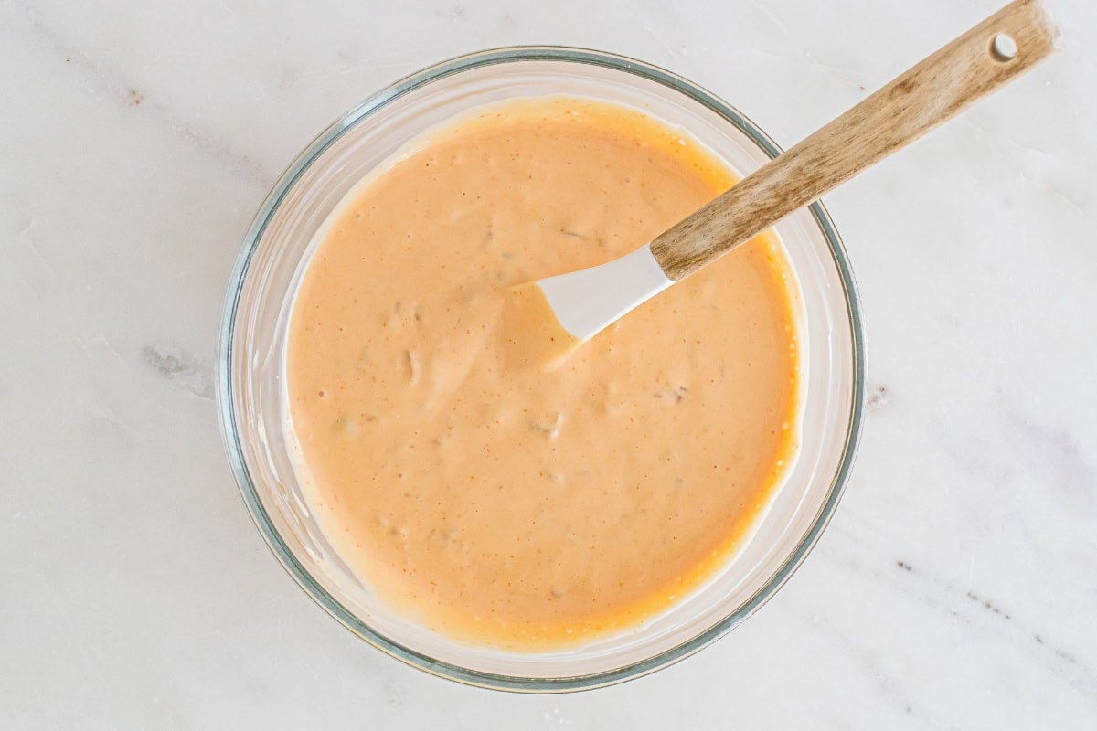 A bowl of creamy orange sauce with a spatula on a marble surface.