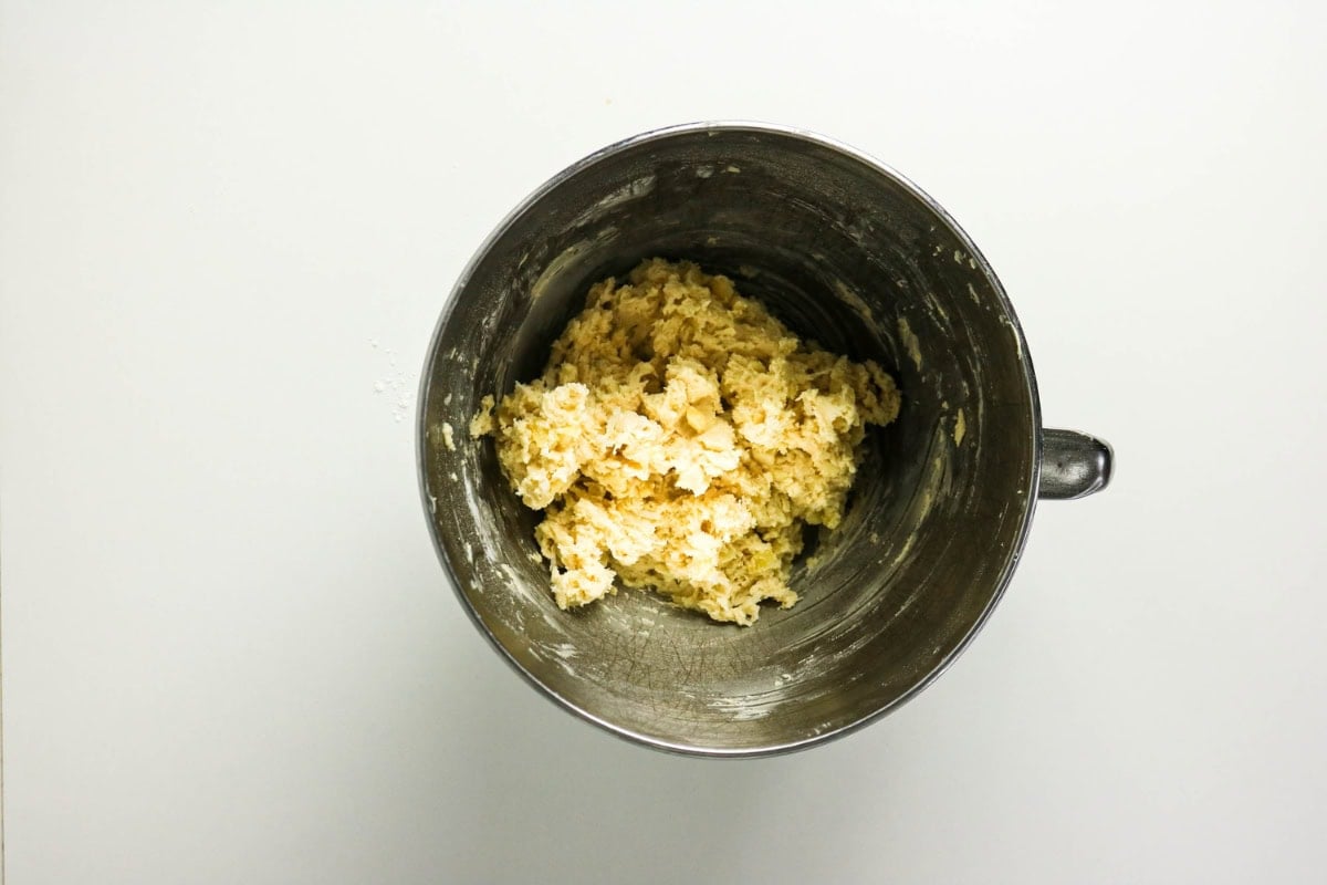 Metal mixing bowl with cookie dough on a white surface, viewed from above.