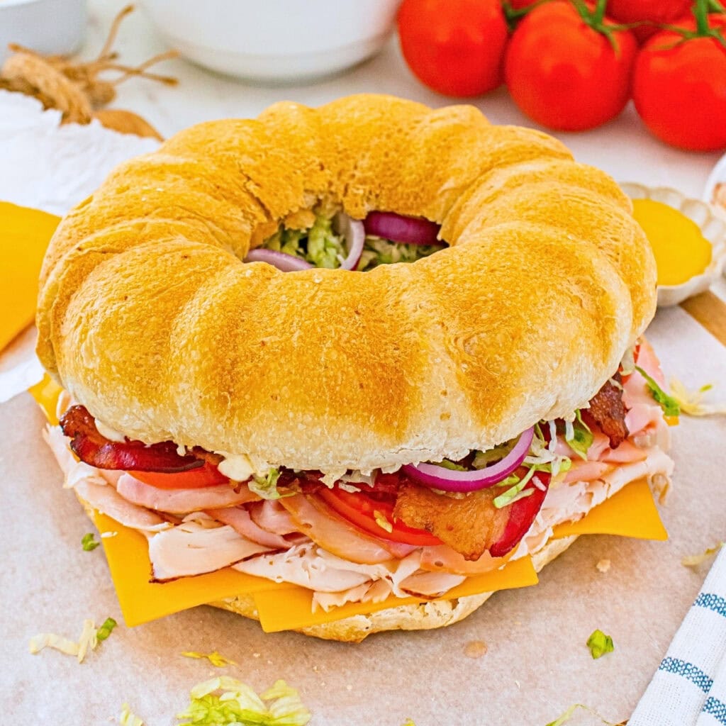 Round sandwich with turkey, cheese, bacon, lettuce, tomato, and onion.