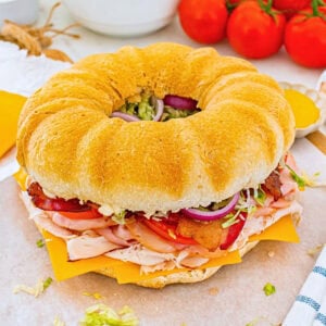 Round sandwich with turkey, cheese, bacon, lettuce, tomato, and onion.