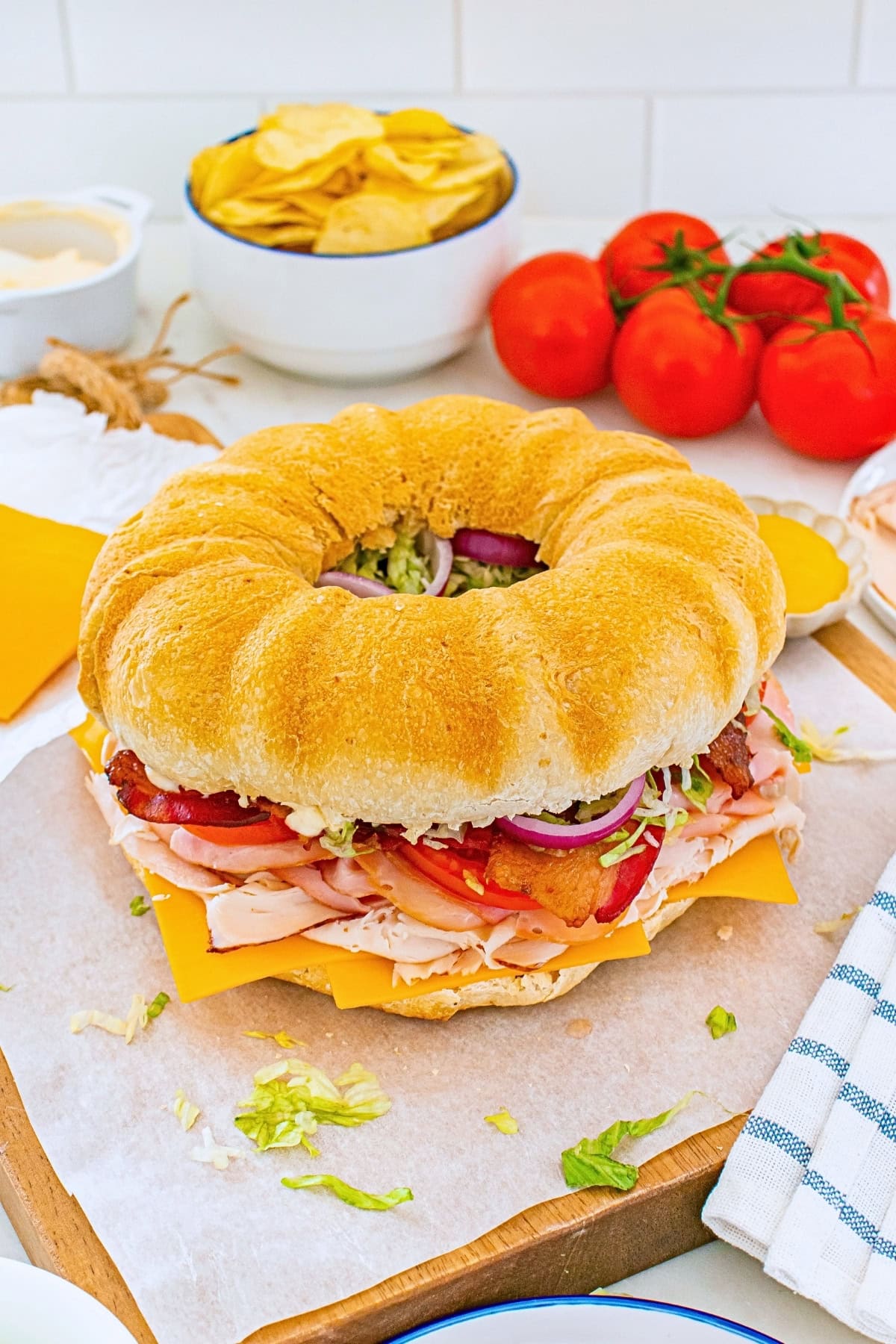 Ring-shaped sandwich with turkey, cheese, bacon, lettuce, and tomato nearby.